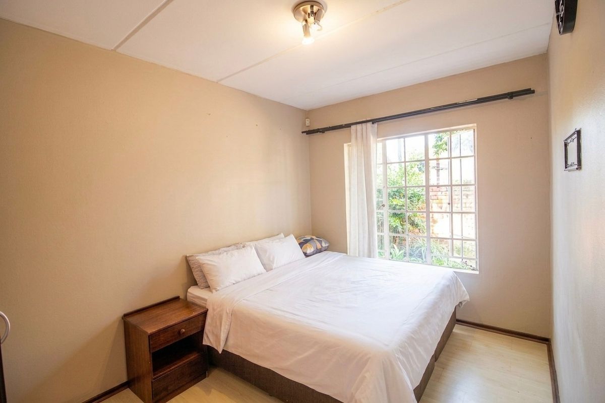 A functional bedroom featuring laminate flooring, a window with security bars, and a ceiling light fixture.