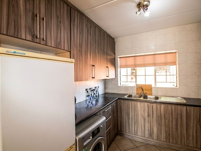 A functional kitchen featuring wood-look laminate cabinetry, dark granite countertops, a double stainless steel sink, and tiled backsplash with integrated appliance space.