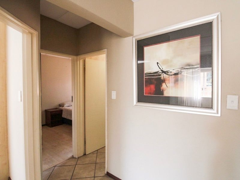 A neutral-toned hallway featuring tiled flooring and an archway leading into a bedroom area.