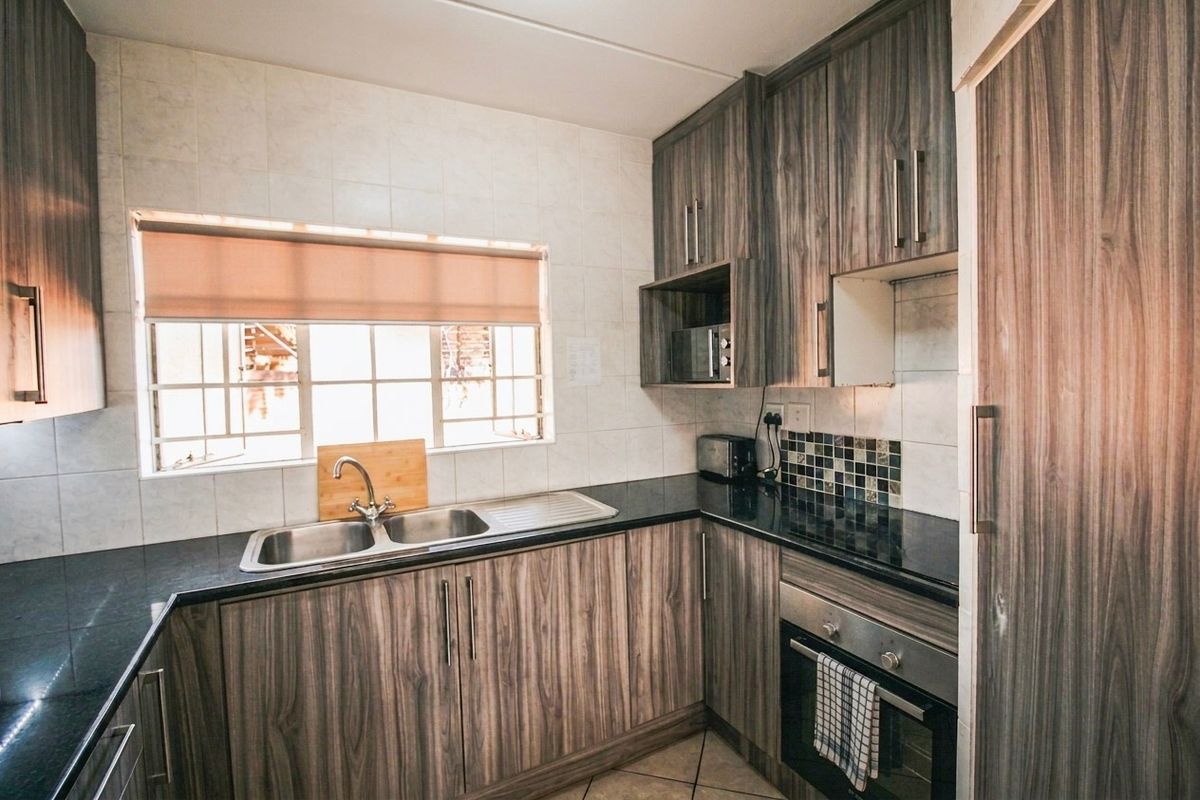 A functional kitchen featuring wood-grain laminate cabinetry, dark granite countertops, a stainless steel double sink, and a built-in oven with tiled backsplash.