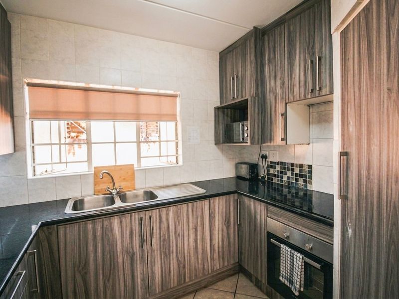 A functional kitchen featuring wood-grain laminate cabinetry, dark granite countertops, a stainless steel double sink, and a built-in oven with tiled backsplash.