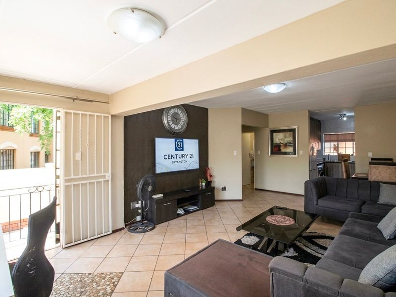 Open-plan living area featuring tiled flooring, a security gate leading to a balcony, and an integrated kitchen space.