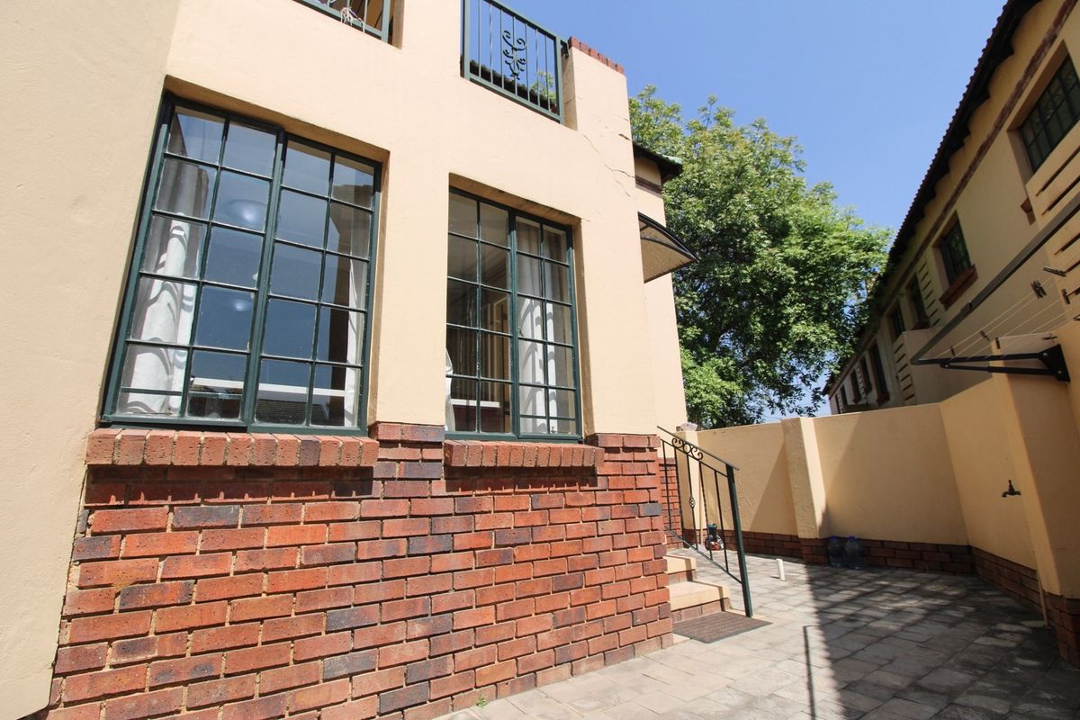 Rear exterior view of the apartment featuring a paved courtyard, brick facade, and steel-framed windows with a small balcony above.