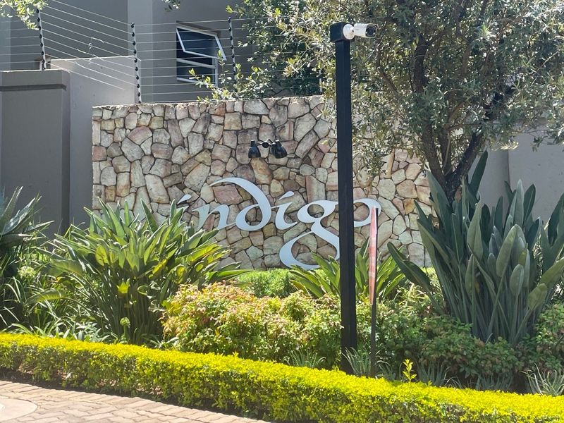 The entrance to the Indigo complex features a decorative stone wall, manicured garden beds, and integrated security infrastructure.