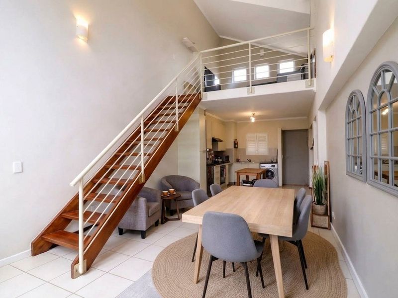 Open-plan living area featuring a timber staircase leading to a mezzanine level, tiled flooring, and an integrated kitchen space.