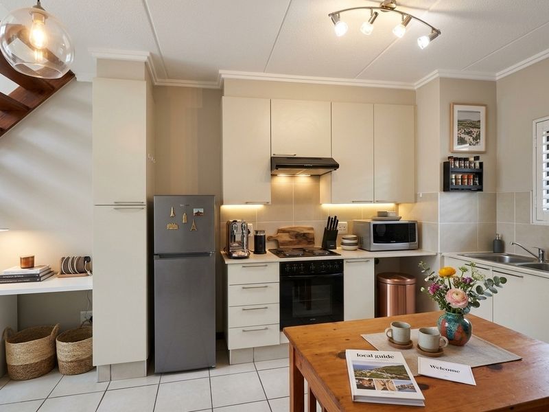 A well-maintained kitchen featuring neutral cabinetry, built-in oven and hob, extractor fan, and tiled flooring, with an adjacent built-in desk area.