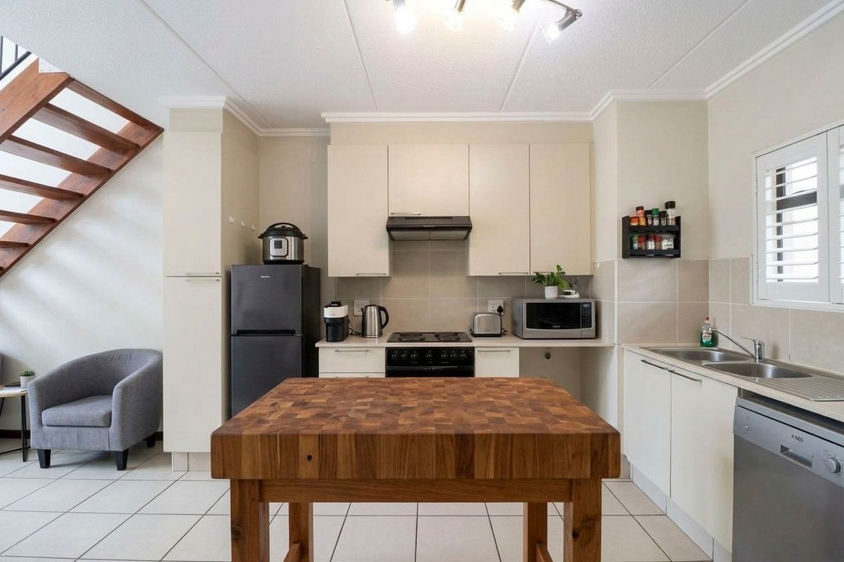 A functional kitchen featuring built-in cabinetry, a hob, extractor fan, and double basin sink, with tiled flooring and an adjacent staircase.