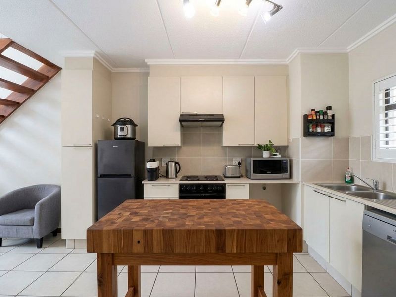 A functional kitchen featuring built-in cabinetry, a hob, extractor fan, and double basin sink, with tiled flooring and an adjacent staircase.