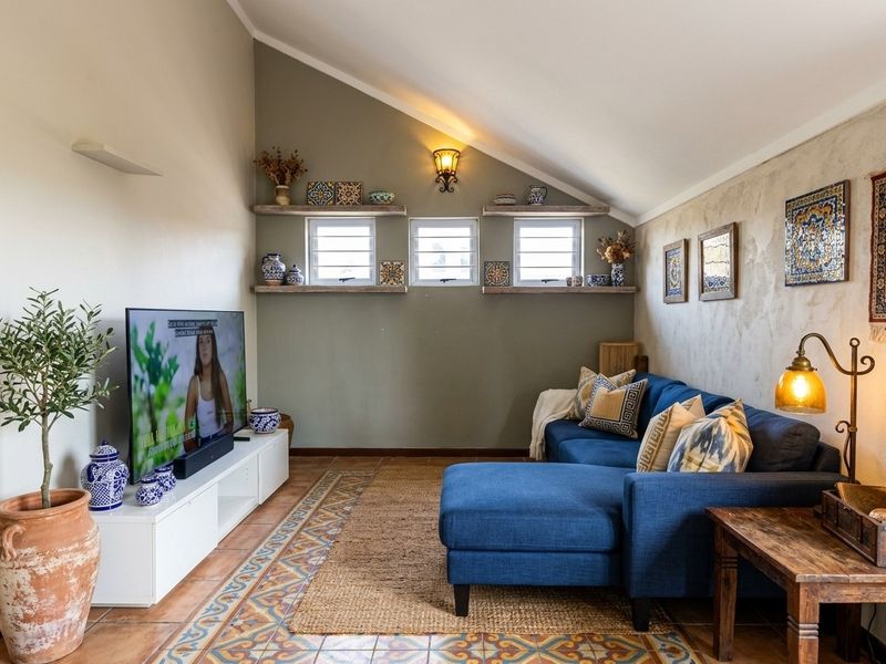 A cozy living room featuring a vaulted ceiling, terracotta flooring with decorative borders, louvered windows, and built-in shelving.