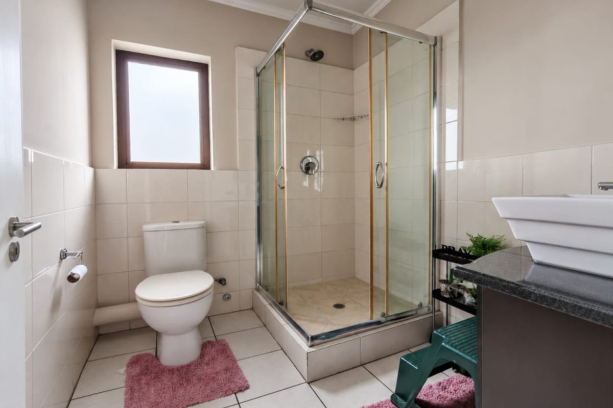 A functional bathroom featuring a glass-enclosed shower, a modern vanity basin, and neutral wall and floor tiling.