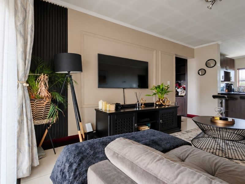 A well-maintained open-plan living area featuring decorative wall molding, tiled floors, and a seamless transition into the adjacent kitchen space.