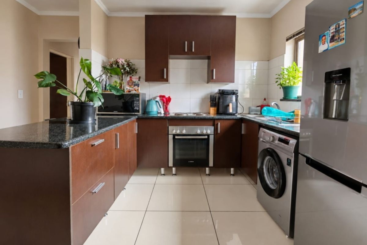 A functional kitchen featuring dark wood cabinetry, granite countertops, tiled flooring, and built-in appliances including an oven and hob.