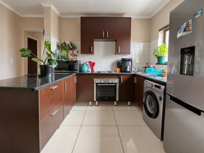 A functional kitchen featuring dark wood cabinetry, granite countertops, tiled flooring, and built-in appliances including an oven and hob.