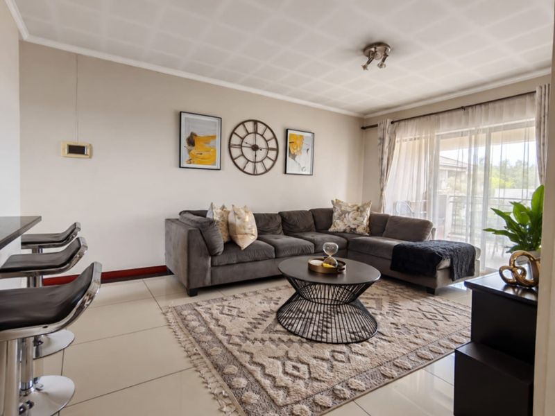 A bright and spacious living room featuring large format floor tiles, a breakfast bar, and a sliding glass door leading to an outdoor area.