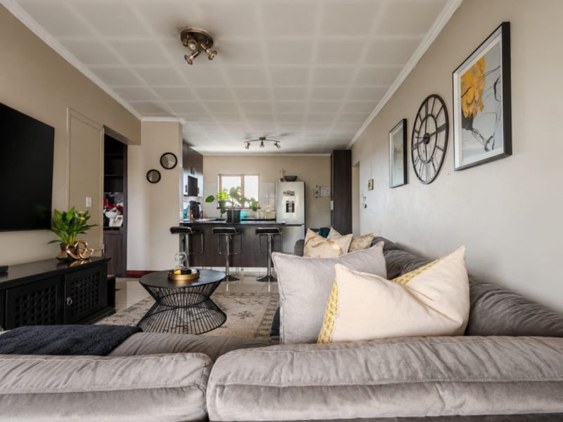 Open-plan living and kitchen area featuring a breakfast bar, neutral wall tones, and textured ceiling tiles, creating a functional and connected living space.