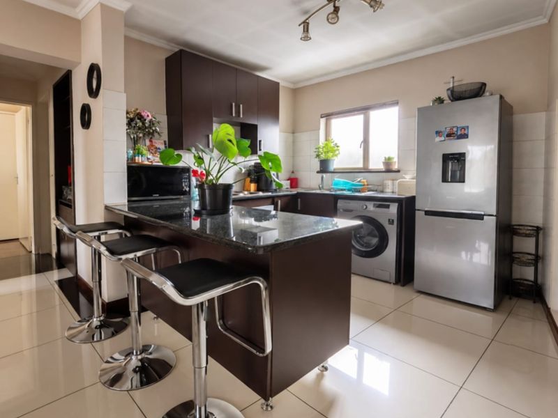 A functional kitchen featuring dark wood cabinetry, granite countertops, tiled flooring, and integrated laundry facilities, providing a practical and well-maintained cooking space.