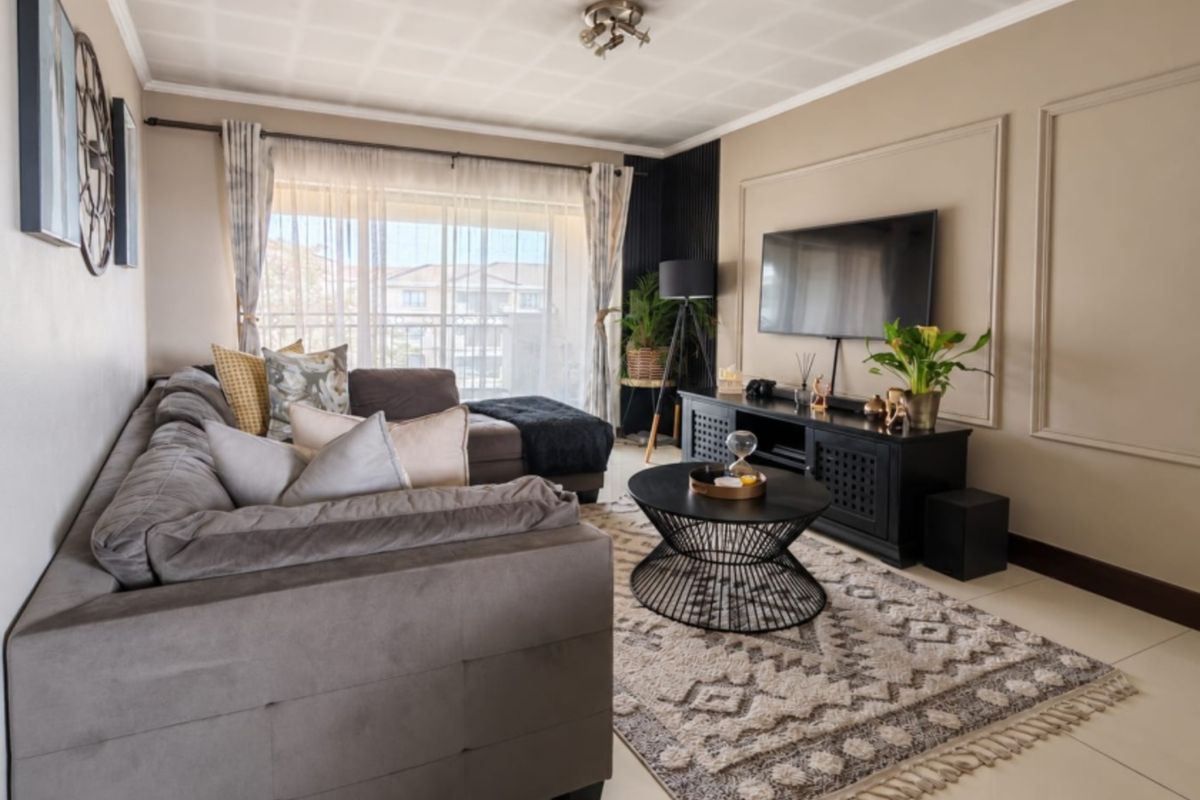 A well-maintained living room featuring tiled flooring, decorative wall molding, and a sliding glass door providing access to the balcony.