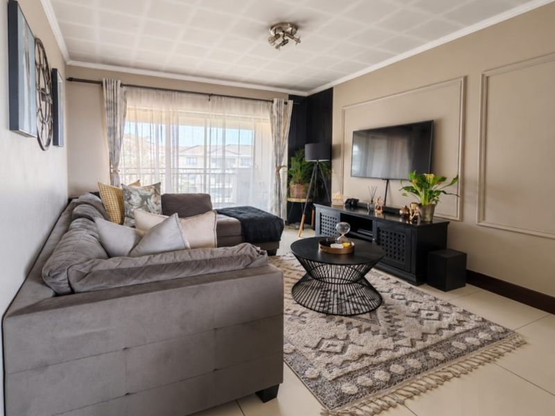 A well-maintained living room featuring tiled flooring, decorative wall molding, and a sliding glass door providing access to the balcony.