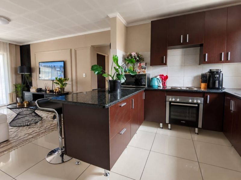 An open-plan living and kitchen area featuring dark wood cabinetry, granite countertops, a kitchen island, and polished tile flooring.