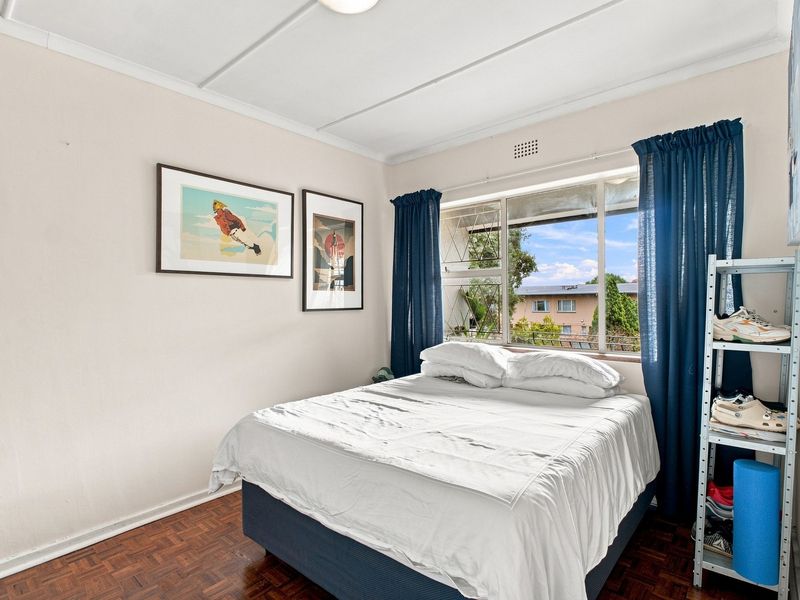 A bedroom featuring parquet flooring, a steel-framed window with security bars, and a ceiling vent, offering a functional space with natural light.