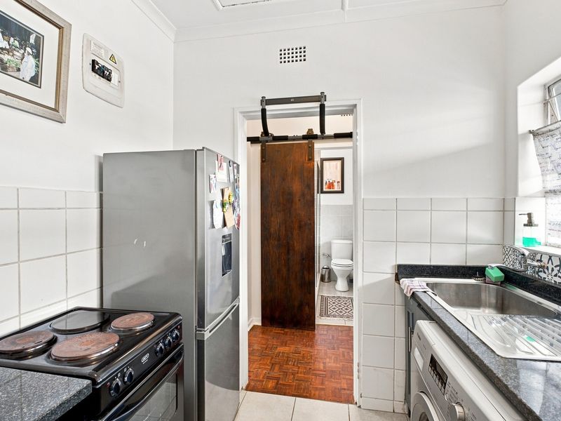 Compact kitchen featuring granite countertops, tiled backsplash, electric stove, and a sliding barn door leading to an adjacent bathroom area.