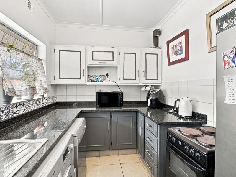 Compact kitchen featuring granite countertops, tiled backsplash, built-in cabinetry, and an electric stove with integrated laundry plumbing.
