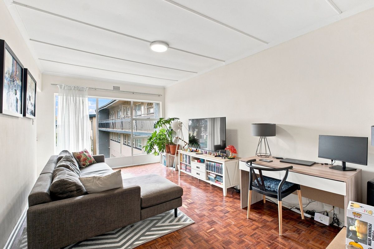 A bright living room featuring classic parquet flooring and a large sliding glass door providing natural light and access to the exterior balcony.