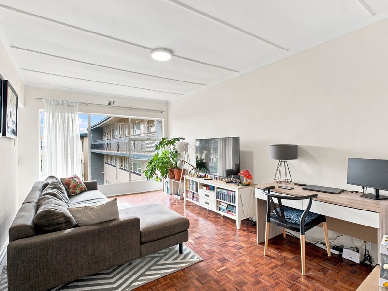 A bright living room featuring classic parquet flooring and a large sliding glass door providing natural light and access to the exterior balcony.