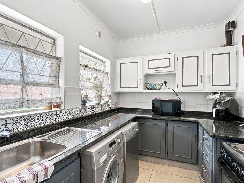A functional kitchen featuring granite countertops, two-tone cabinetry, tiled backsplash, and integrated space for laundry appliances.