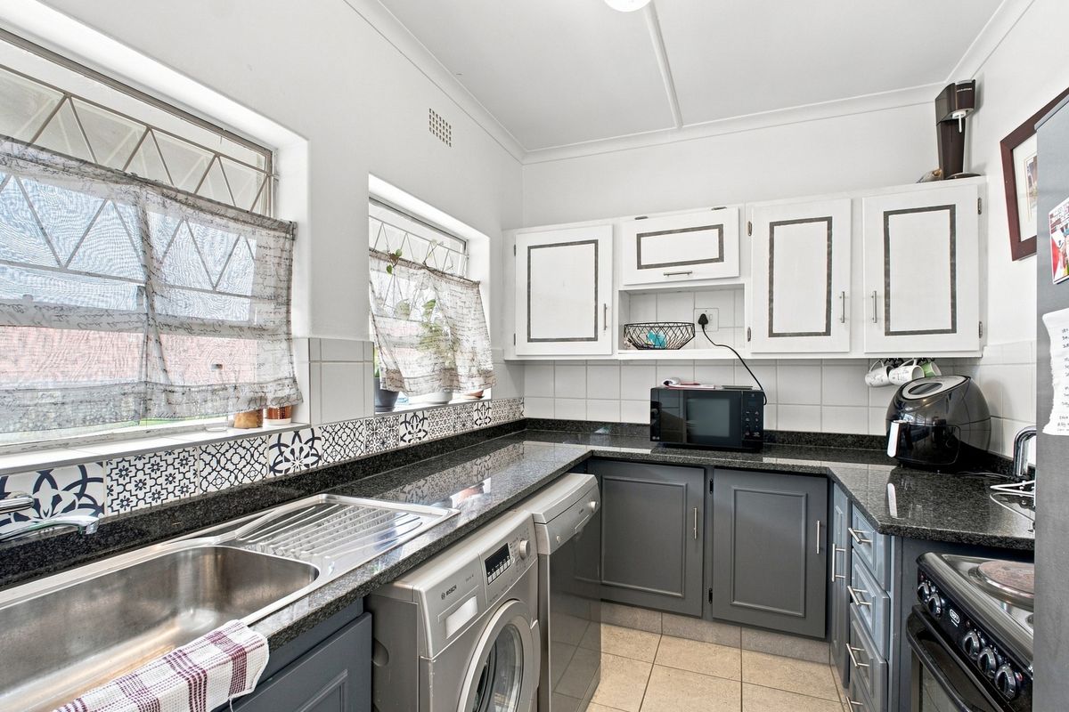 A functional kitchen featuring granite countertops, two-tone cabinetry, tiled backsplash, and integrated space for laundry appliances.