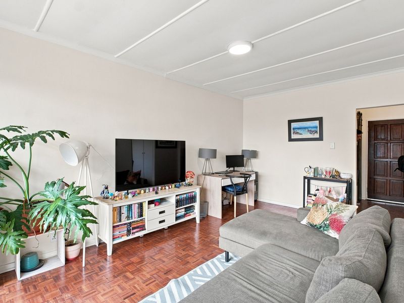A living room featuring classic parquet flooring and a panelled ceiling, providing a functional and well-lit space.
