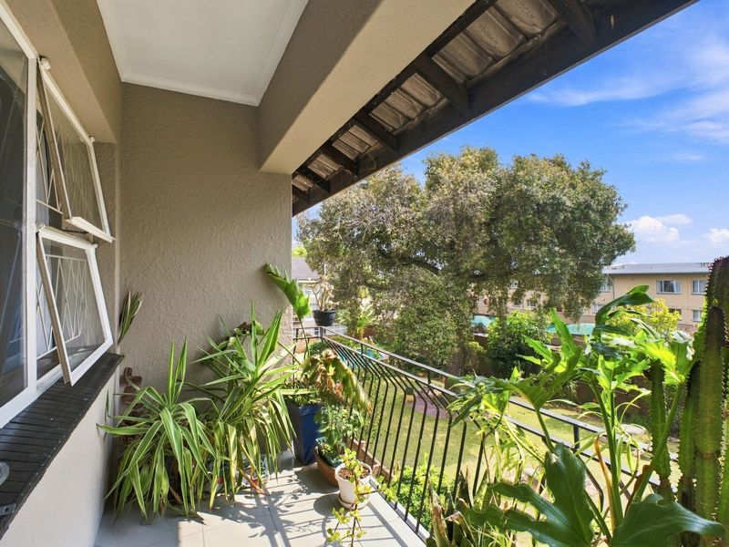 A covered balcony featuring tiled flooring, a metal balustrade, and views over the surrounding garden and neighborhood.