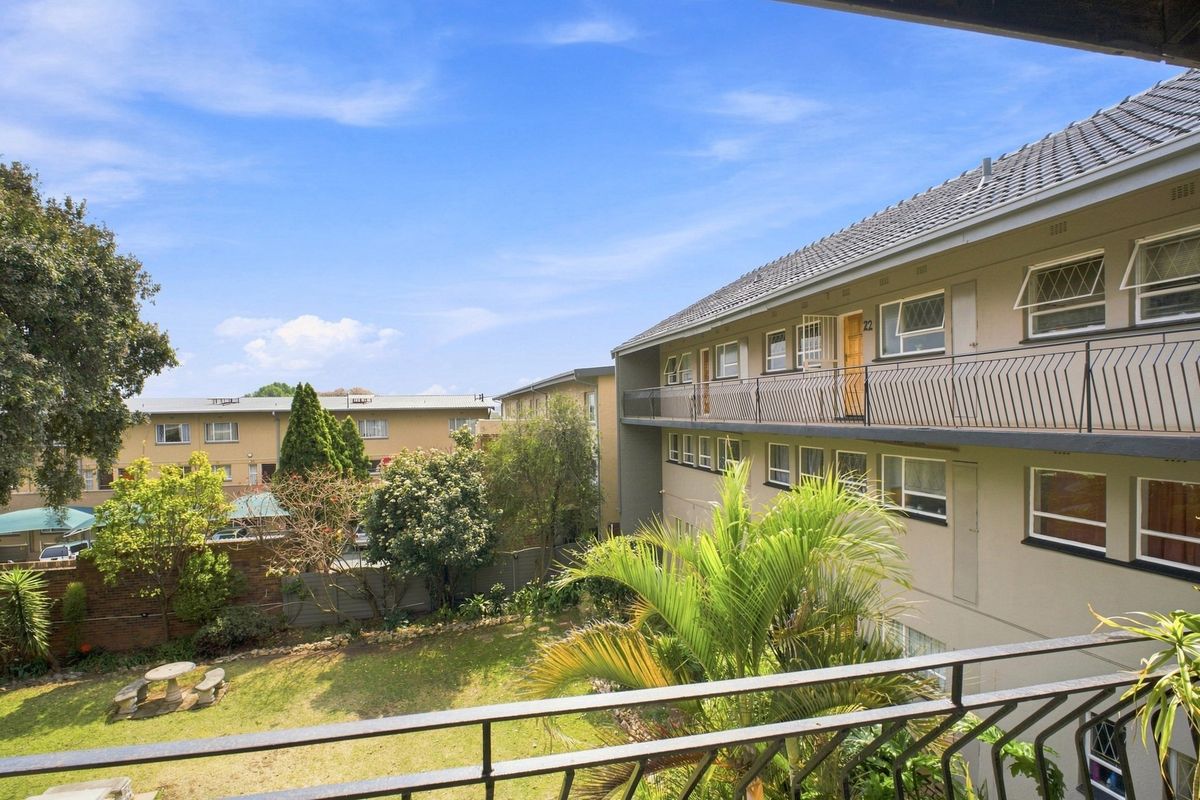 View of the apartment complex exterior, featuring a communal garden area and balcony access to upper-level units.