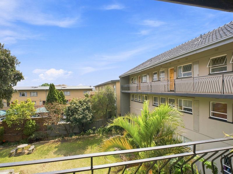 View of the apartment complex exterior, featuring a communal garden area and balcony access to upper-level units.