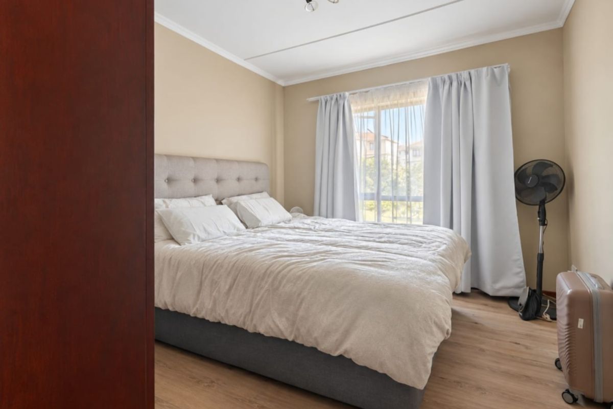 A well-lit bedroom featuring laminate flooring, neutral wall tones, and a large window allowing for natural light.