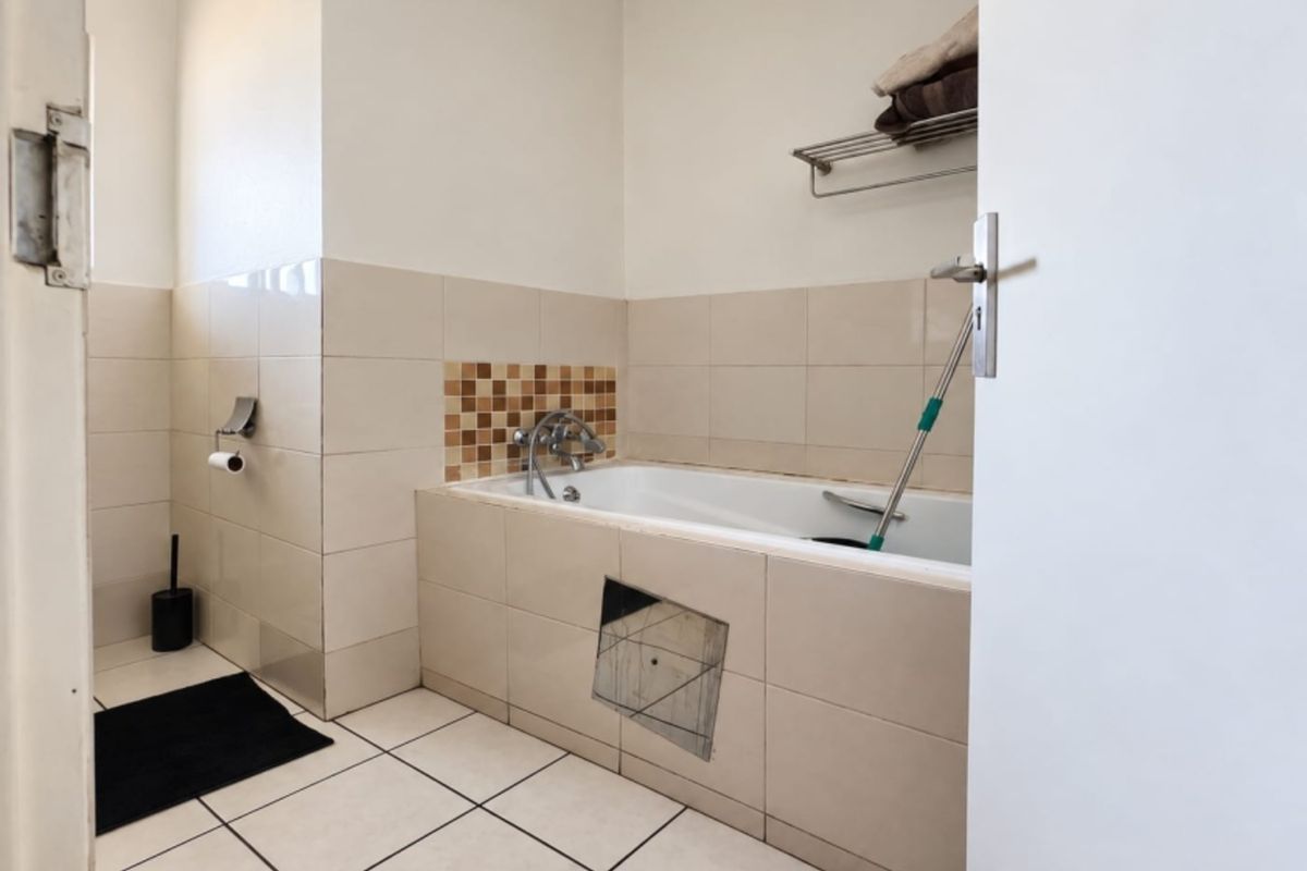 A functional bathroom featuring a built-in bathtub with tiled surround, wall-mounted towel rack, and neutral ceramic floor tiles.