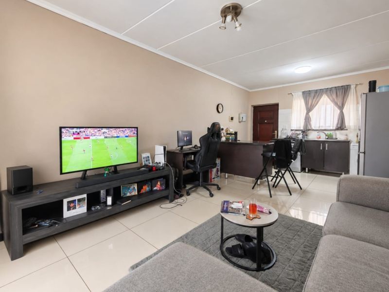 Open-plan living area featuring tiled flooring, a compact kitchen with built-in cabinetry, and direct access to the entrance.