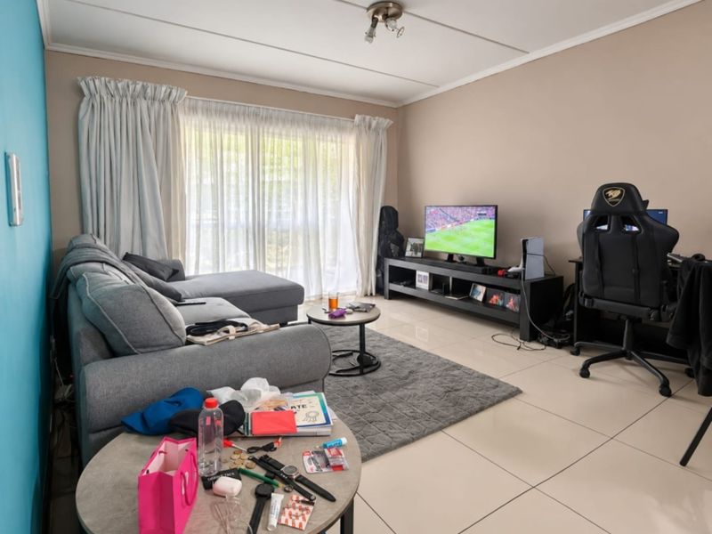 A living room featuring large format floor tiles, a sliding glass door with curtains, and neutral wall finishes.