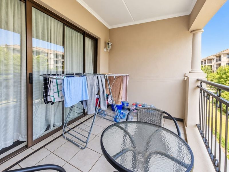 A covered balcony featuring tiled flooring, a metal balustrade, and a sliding glass door providing access to the interior living space.
