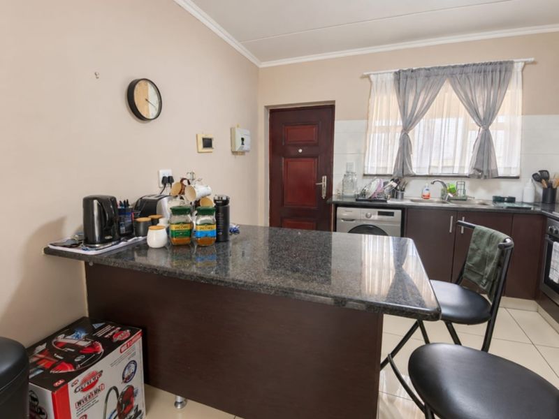 A functional kitchen featuring dark wood cabinetry, granite countertops, a built-in oven, and an integrated washing machine with tiled flooring throughout.