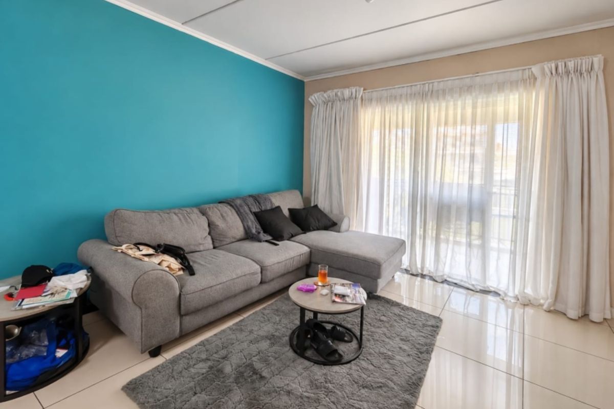 A living room featuring large format floor tiles, a vibrant blue accent wall, and a sliding glass door providing access to an outdoor area.