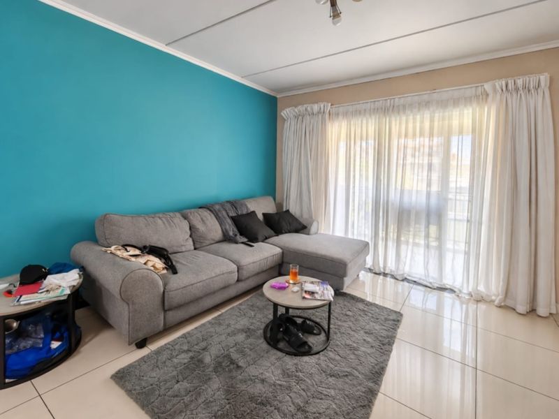 A living room featuring large format floor tiles, a vibrant blue accent wall, and a sliding glass door providing access to an outdoor area.