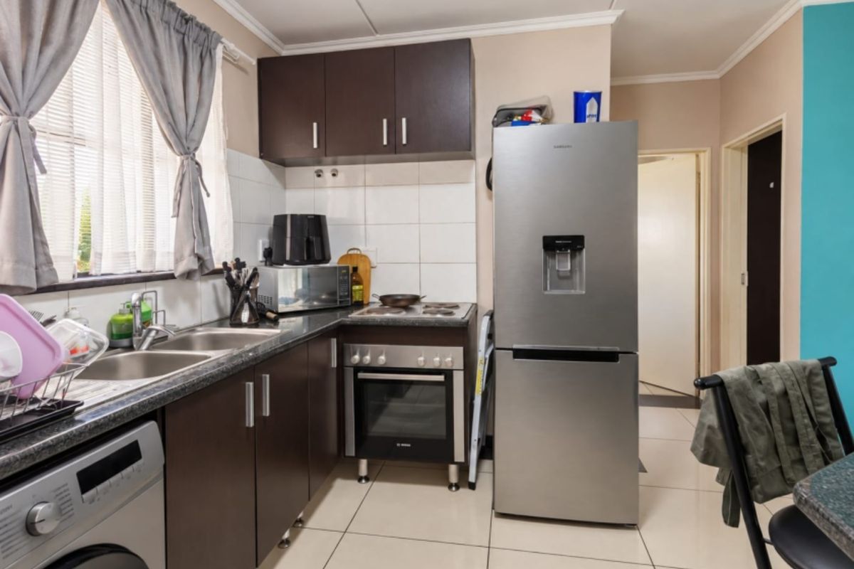 A functional kitchen featuring dark cabinetry, tiled backsplash, double basin sink, and a freestanding oven with hob, finished with neutral floor tiles.
