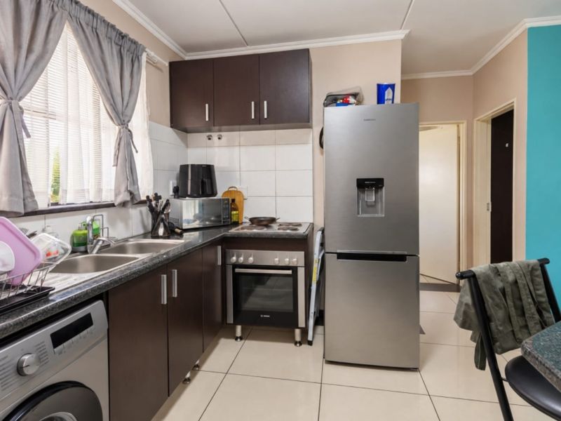 A functional kitchen featuring dark cabinetry, tiled backsplash, double basin sink, and a freestanding oven with hob, finished with neutral floor tiles.