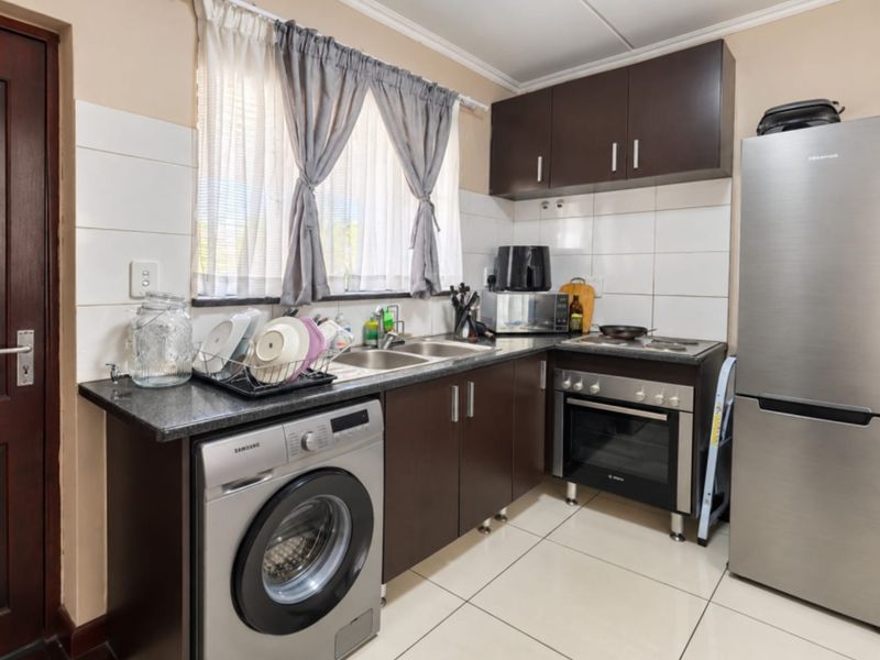 Compact kitchen featuring dark wood cabinetry, granite countertops, tiled backsplash, and integrated oven with hob, providing a functional workspace.