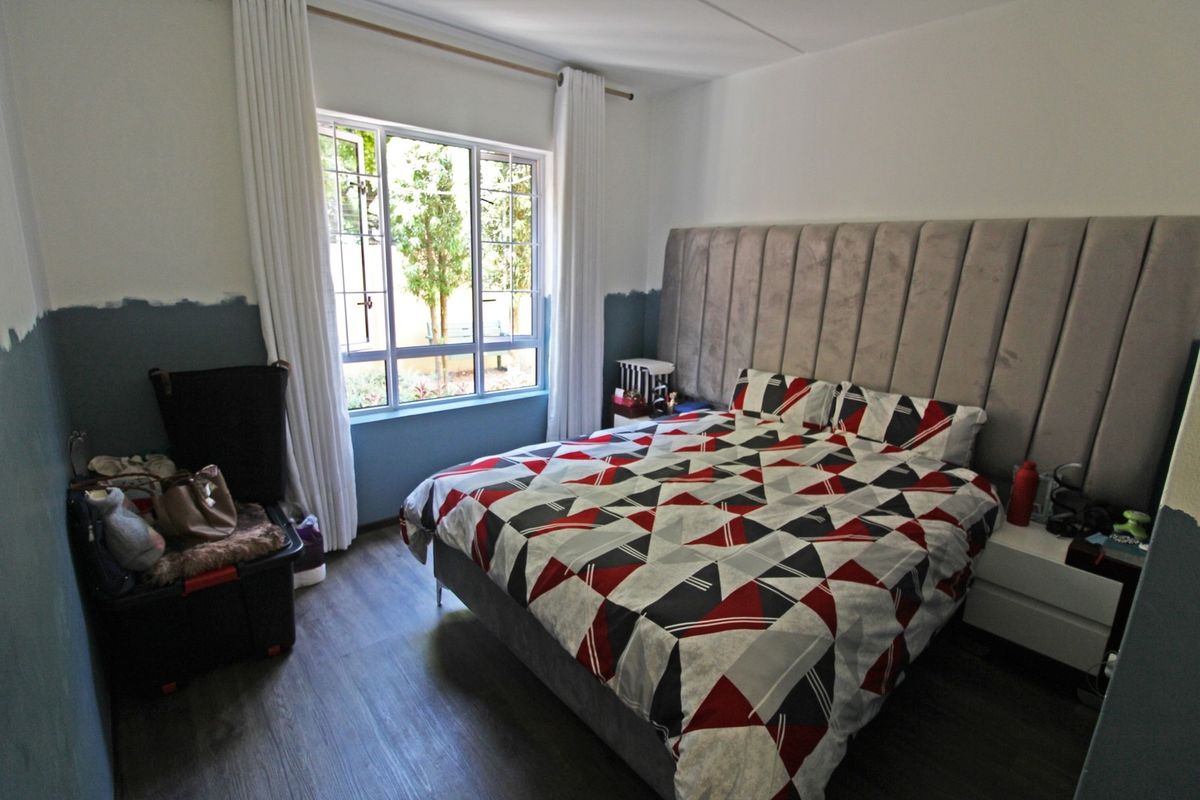 A bedroom featuring laminate flooring and a large window with curtain tracks, currently undergoing wall painting.