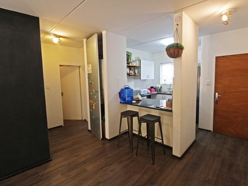 Open plan living area featuring a compact kitchen with a breakfast bar, dark laminate flooring, and neutral wall finishes.