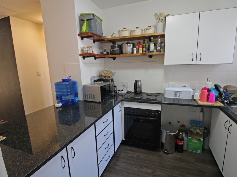 Compact kitchen featuring granite countertops, built-in oven with electric hob, white cabinetry, and open shelving for storage.