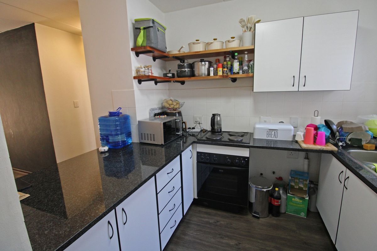 Compact kitchen featuring granite countertops, built-in oven with electric hob, white cabinetry, and open shelving for storage.