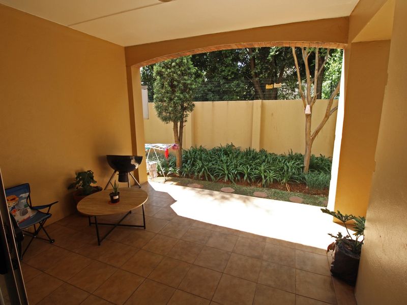A covered patio area featuring tiled flooring and a brick archway, overlooking a private garden space with a boundary wall.
